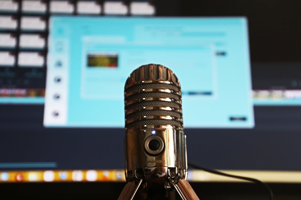 Close-up of a microphone with a blurred computer screen in the background, ideal for podcast themes.