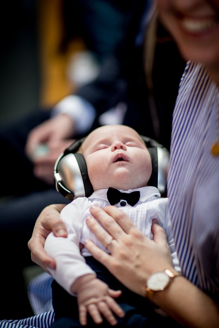 A cute baby wearing headphones and a bow tie sleeping peacefully in an indoor setting.